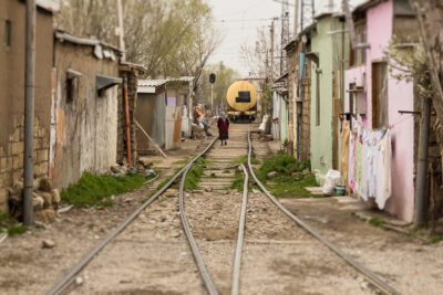 An elderly woman walking down the train tracks running through her neighbourhood: Shanghai, Baku, Azerbaijan.
