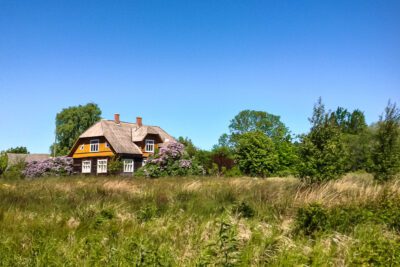 A pretty yellow Latvian traditional house surrounded by land.