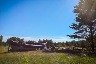 A fishing boat left out in a field under the scorching sun.