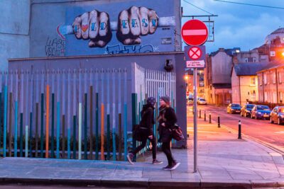 Two pedestrians crossing paths in front of graffiti of double fists in Dublin, Ireland. © 2016 Nicholas Orloff